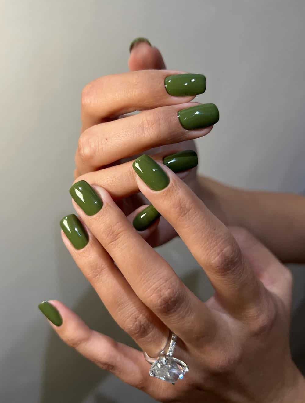image of a hand with square-shaped glossy olive green nails