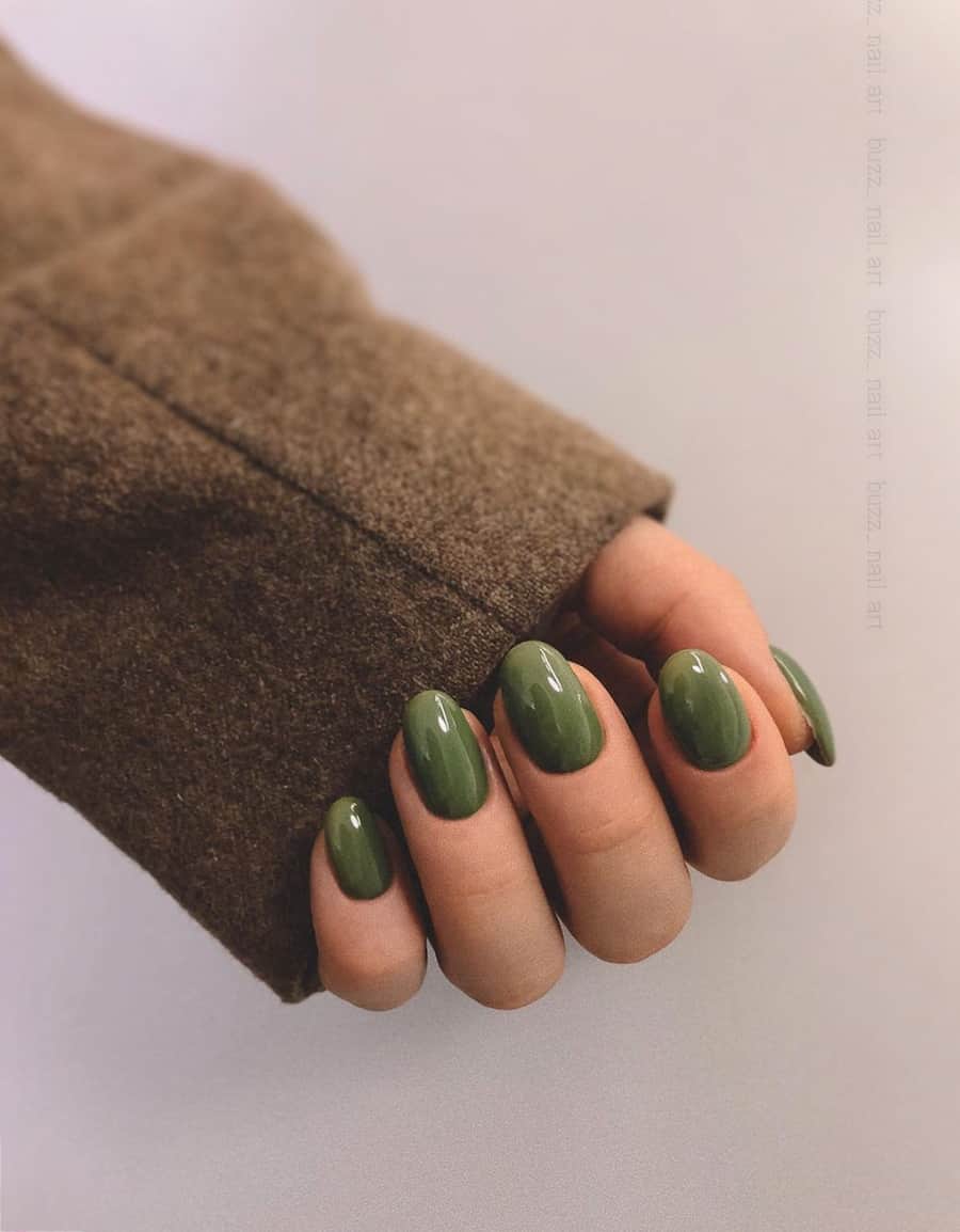 Mano con uñas redondeadas con esmalte verde oliva oscuro.