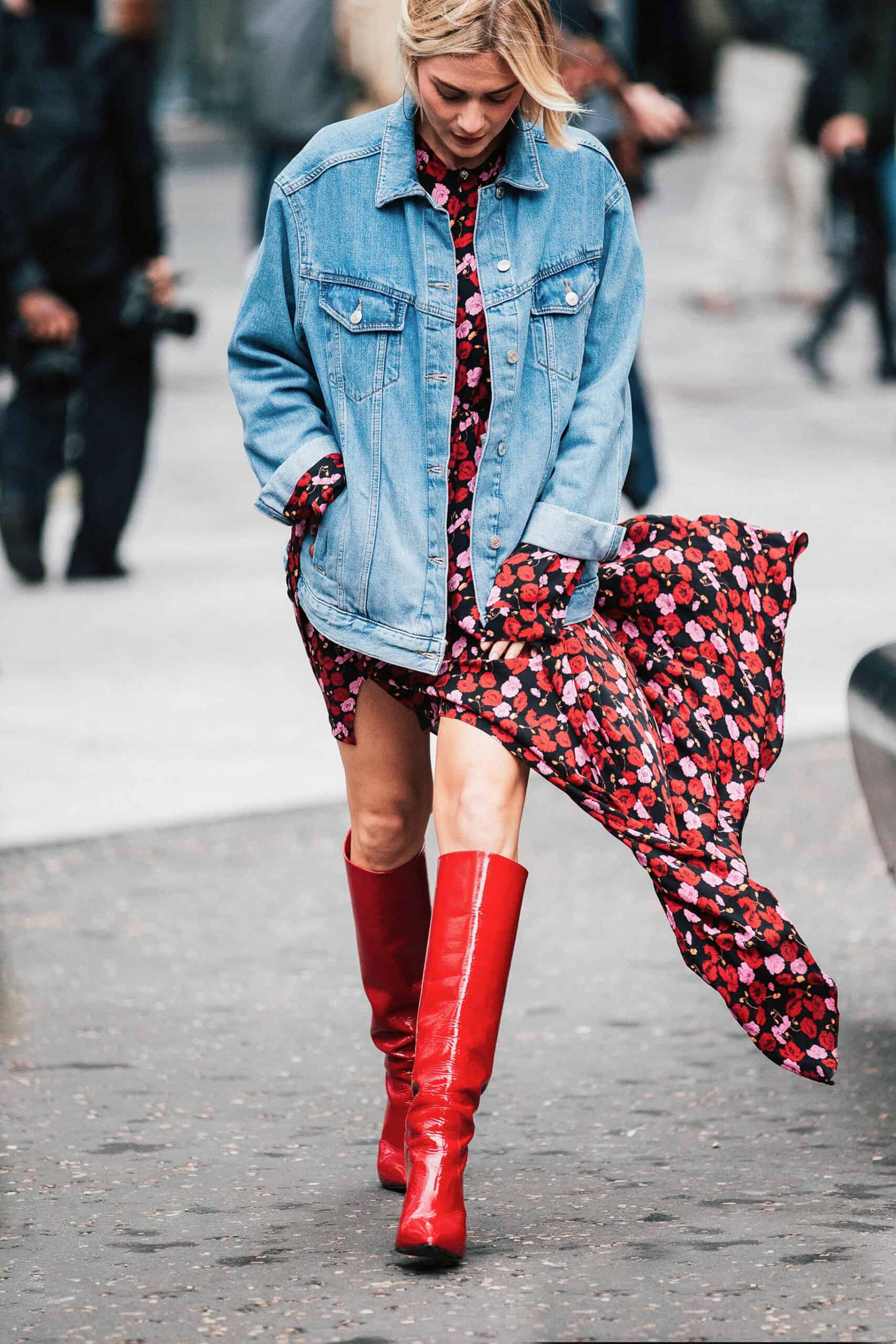 woman wearing an oversized denim jacket over a floral black and red dress with leather knee-high red boots