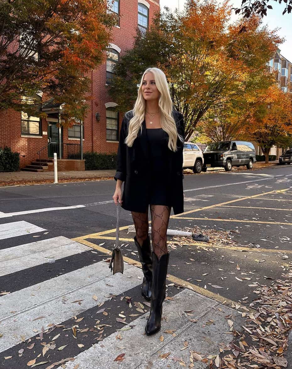 woman wearing a black blazer and mini dress with printed black tights and knee-high boots