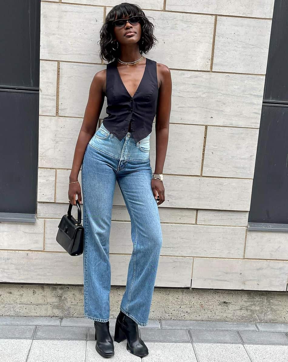 black woman in a sexy black vest top, blue jeans, and boots