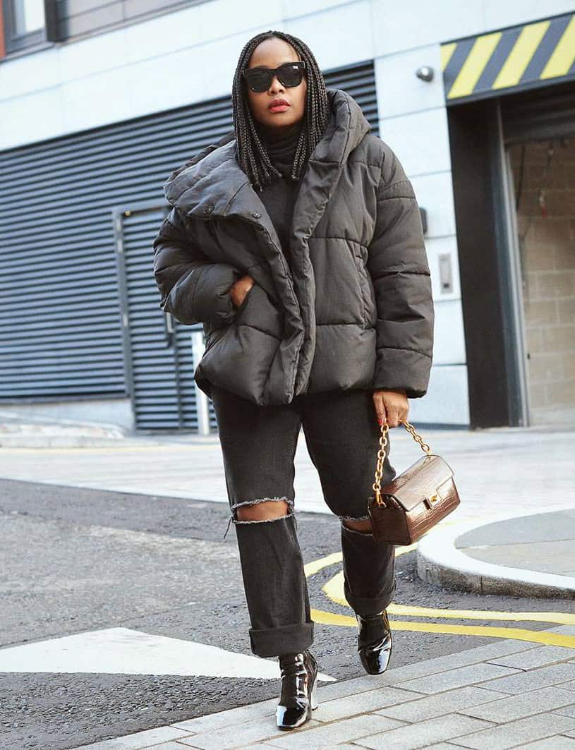 black woman wearing a black puffer coat with ripped jeans and leather boots
