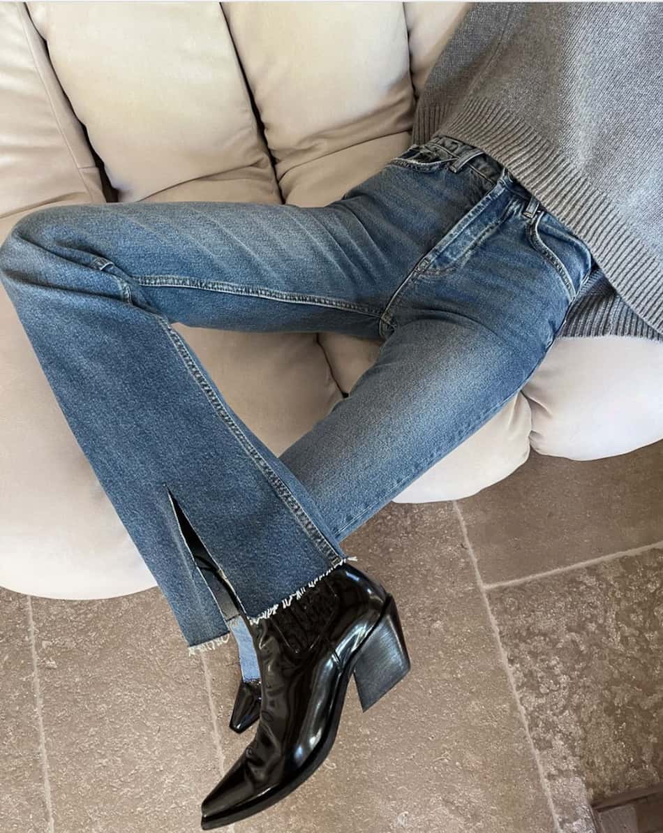 image of a woman from the chest down on a chair wearing a grey sweater, jeans, and black boots