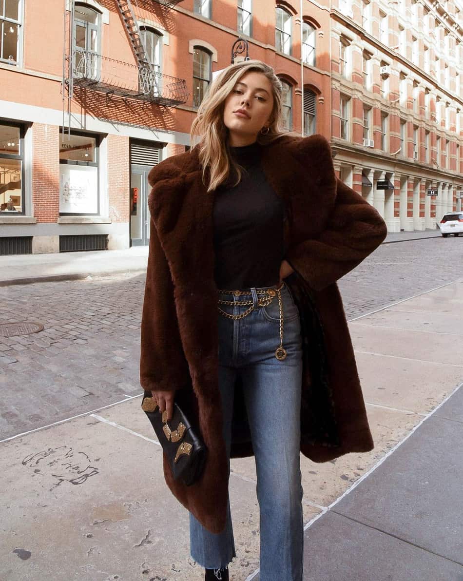 woman wearing a faux fur brown coat with a black turtleneck sweater and jeans