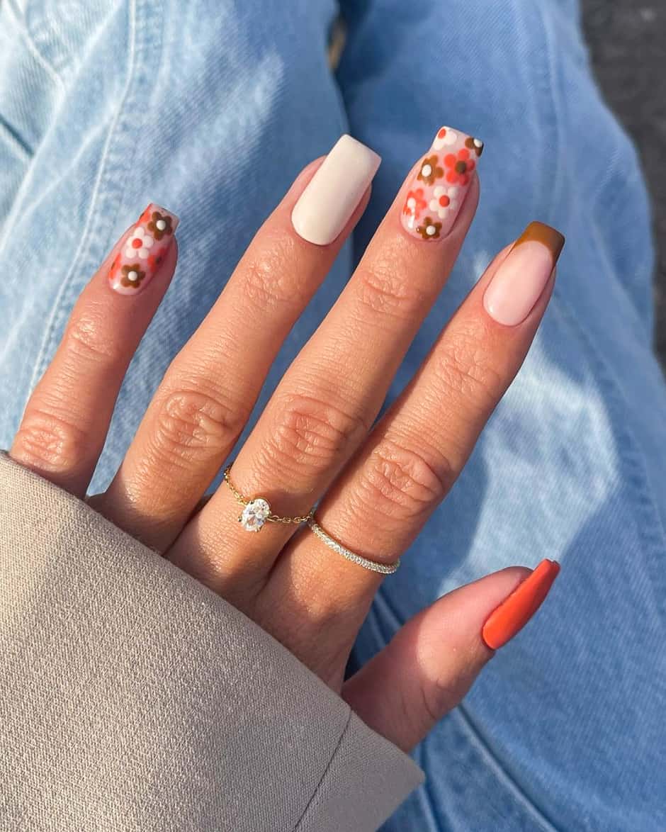 image of a hand with 70s inspired nails with brown, orange and cream flowers and french tips