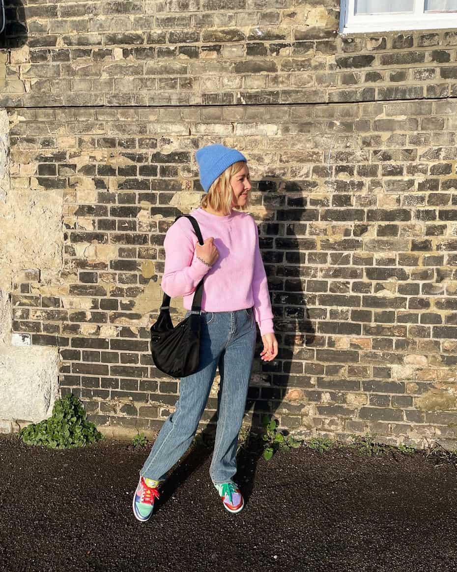 woman wearing a blue beanie, baby pink sweater, blue jeans, and colorblock sneakers