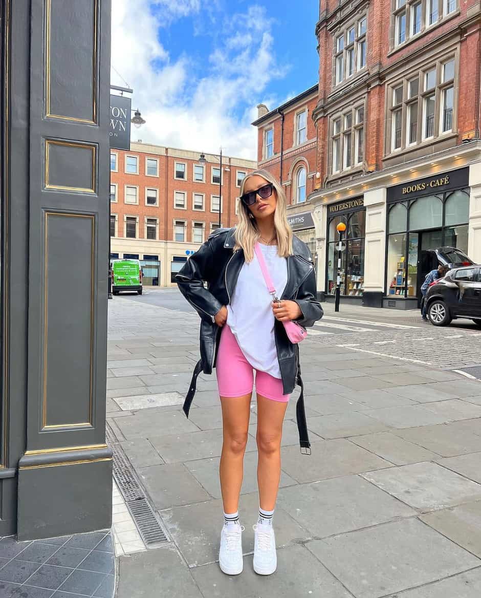 Woman wearing hot pink biker shorts, a white t-shirt, a leather jacker and sneakers.