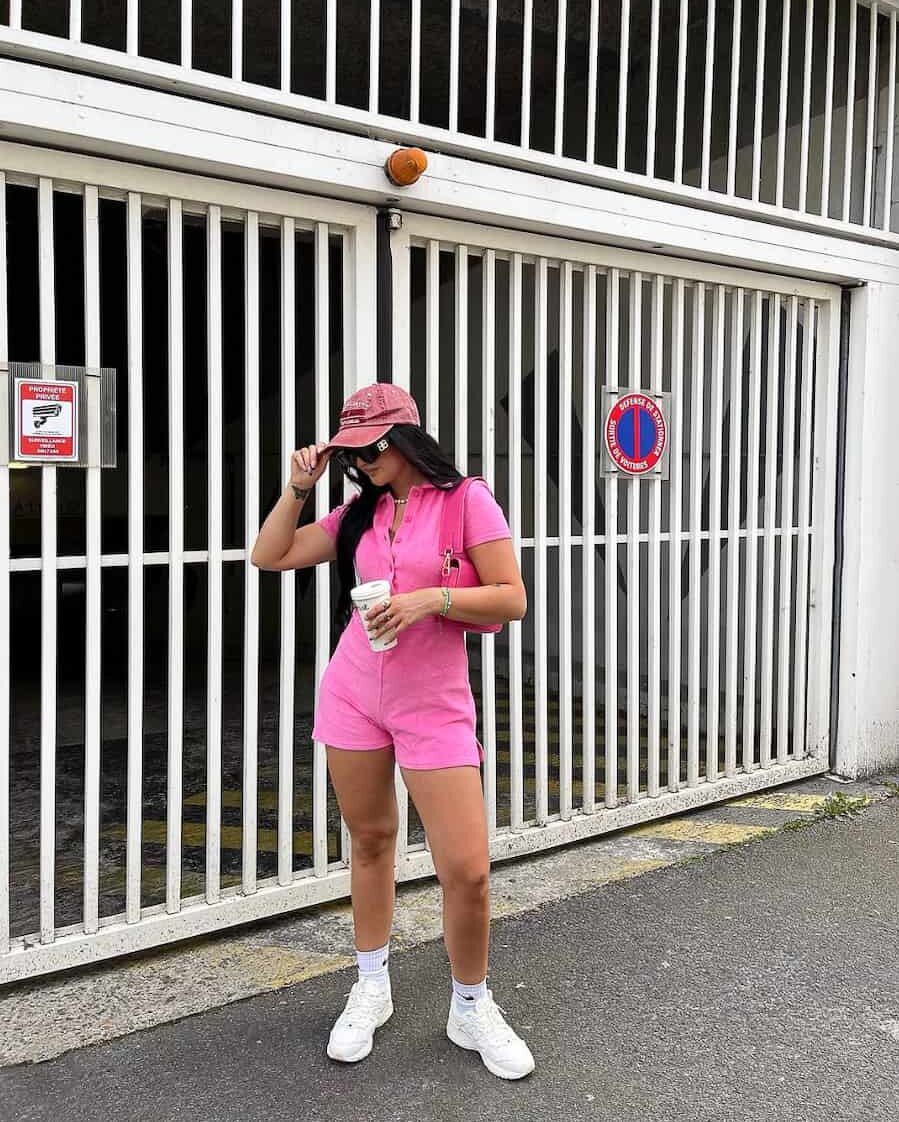 Woman wearing a hot pink romper, pink hat and white sneakers.