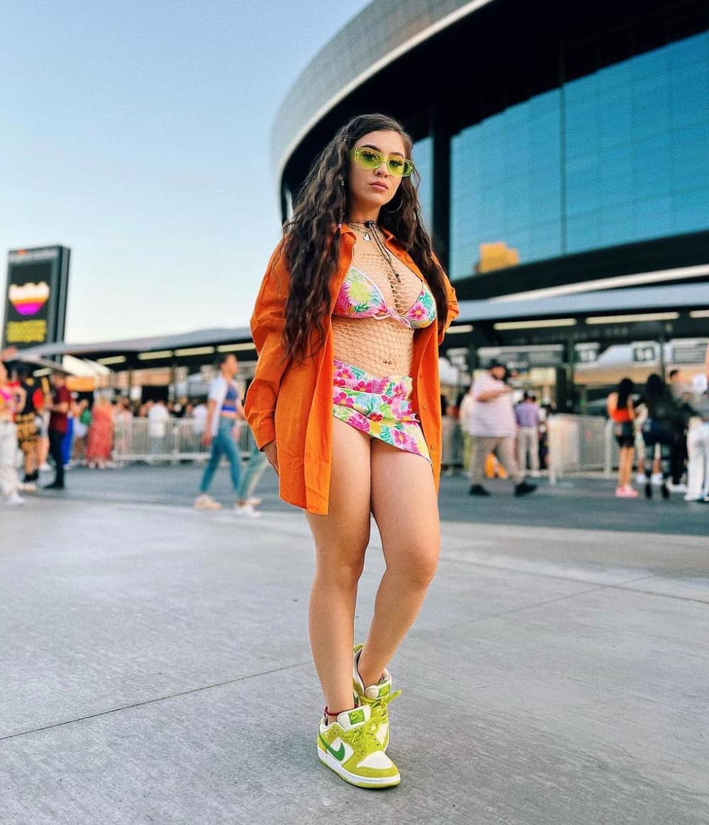 Woman wearing an orange button up over a floral bikini and sneakers.