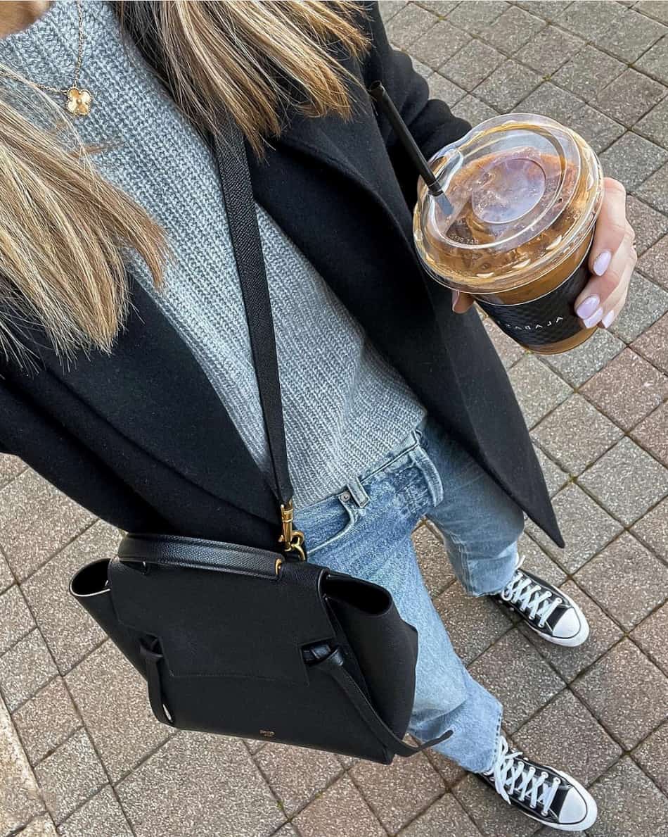 overhead selfie of a woman in a black blazer, grey knit sweater, blue jeans, and black converse sneakers