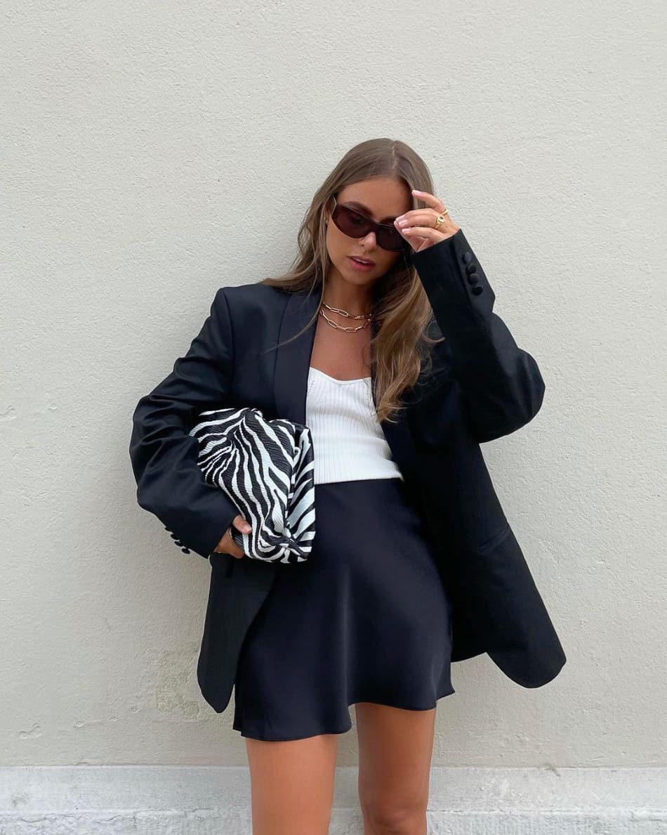 woman wearing an oversized black blazer with a knit white strapless top and a mini length black slip skirt