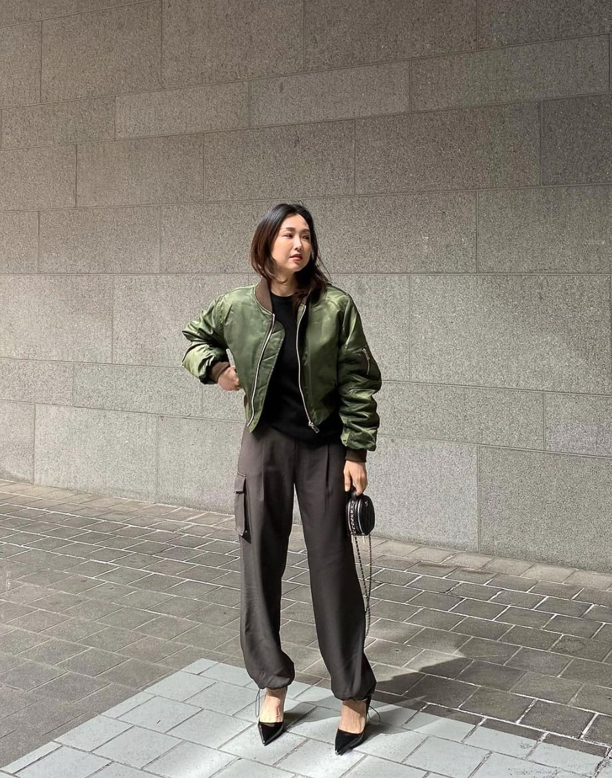 woman wearing a satin green bomber jacket with faded black silk joggers and black pumps