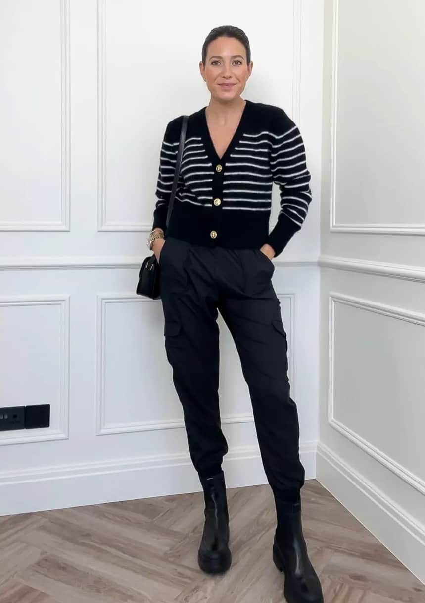 woman wearing a black striped cardigan with gold buttons, black joggers, and black lug boots