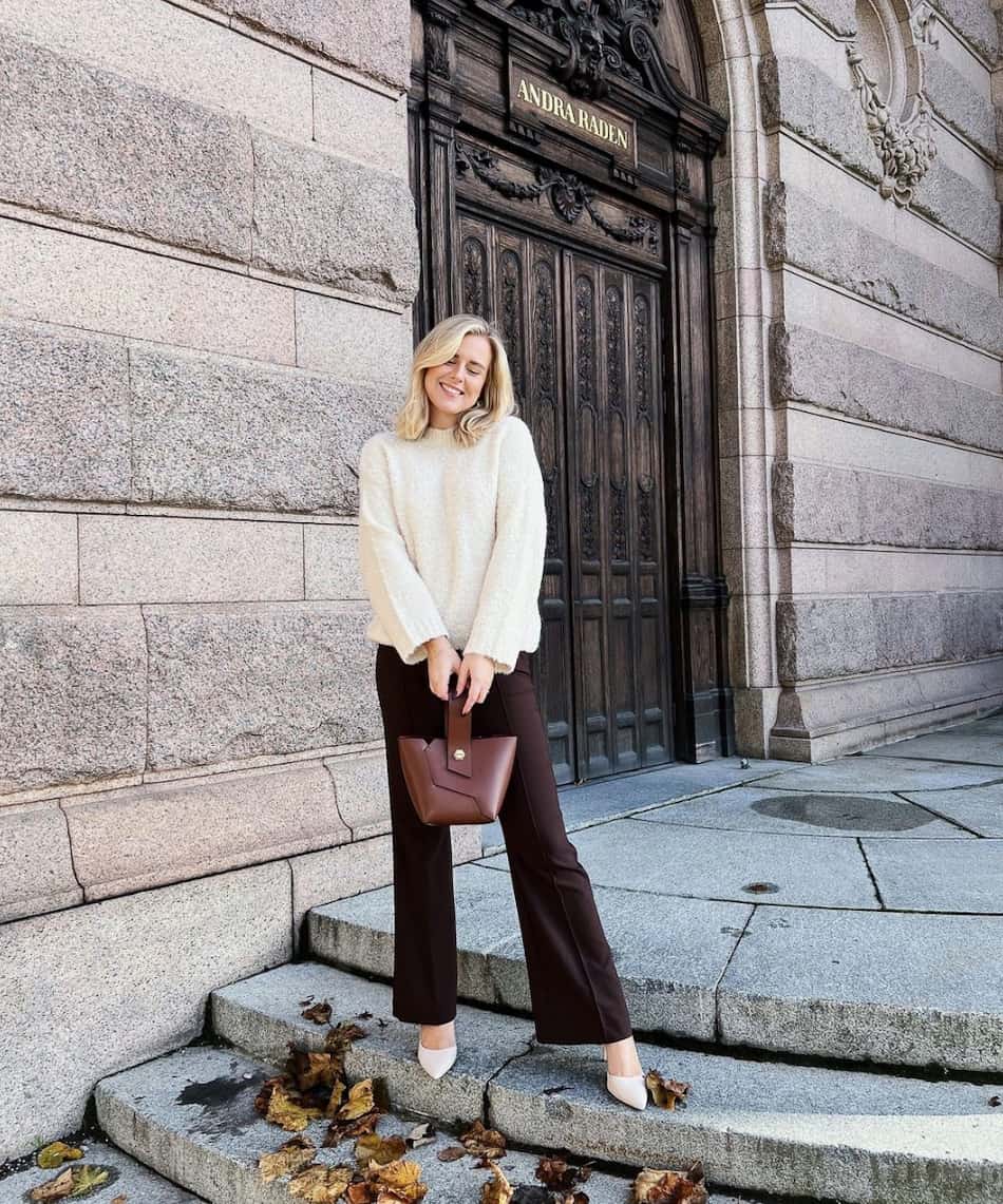 woman wearing an ivory mock neck sweater with brown flared pants and white pumps
