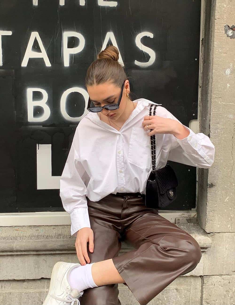 woman wearing a white button down shirt with brown leather pants and white sneakers