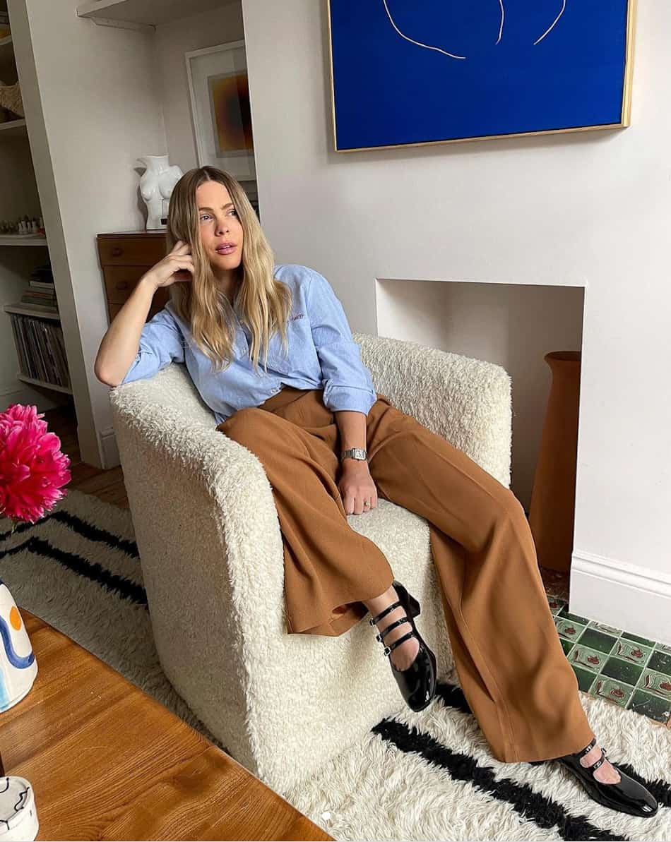 woman wearing a light blue button up shirt with camel brown trousers and black patent leather Mary Jane shoes