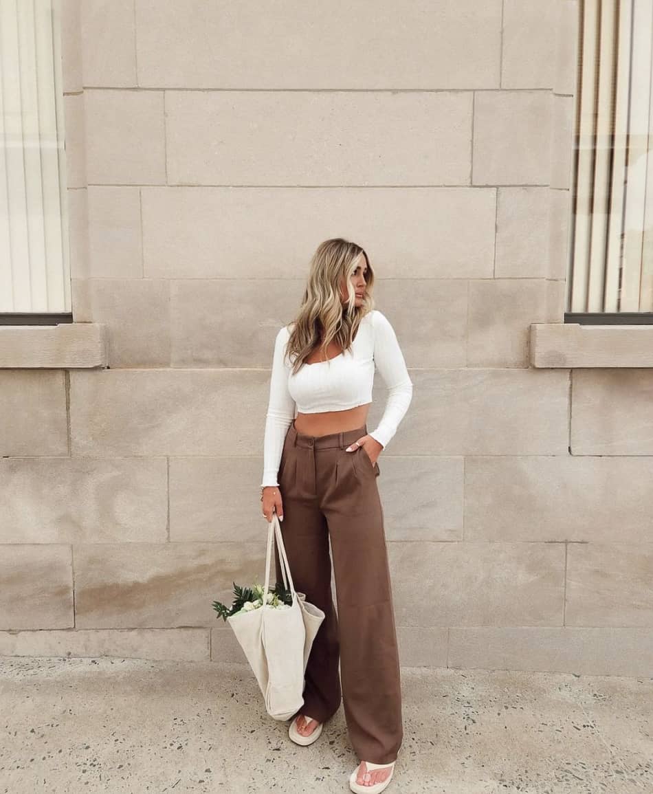 woman wearing a cropped long sleeve white top with wide leg brown pants and white sandals