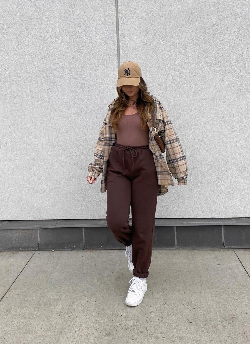 woman wearing a plaid brown shirt with a brown tank and brown sweatpants and white sneakers