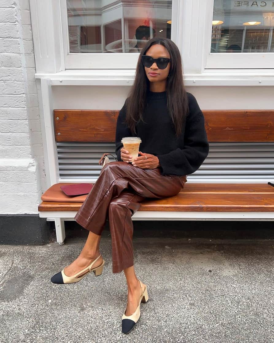 Black woman wearing a black pullover sweater with brown croc effect leather pants and Chanel slingback heels