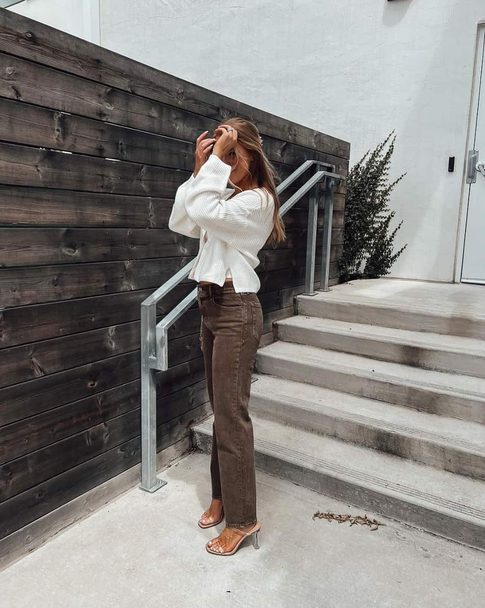 woman wearing a cream cardigan with brown jeans and clear pumps