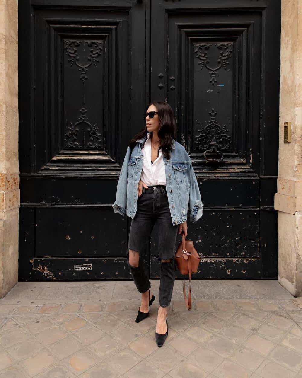woman wearing an oversized denim jacket with a white button up shirt, black jeans, and low black slingback heels