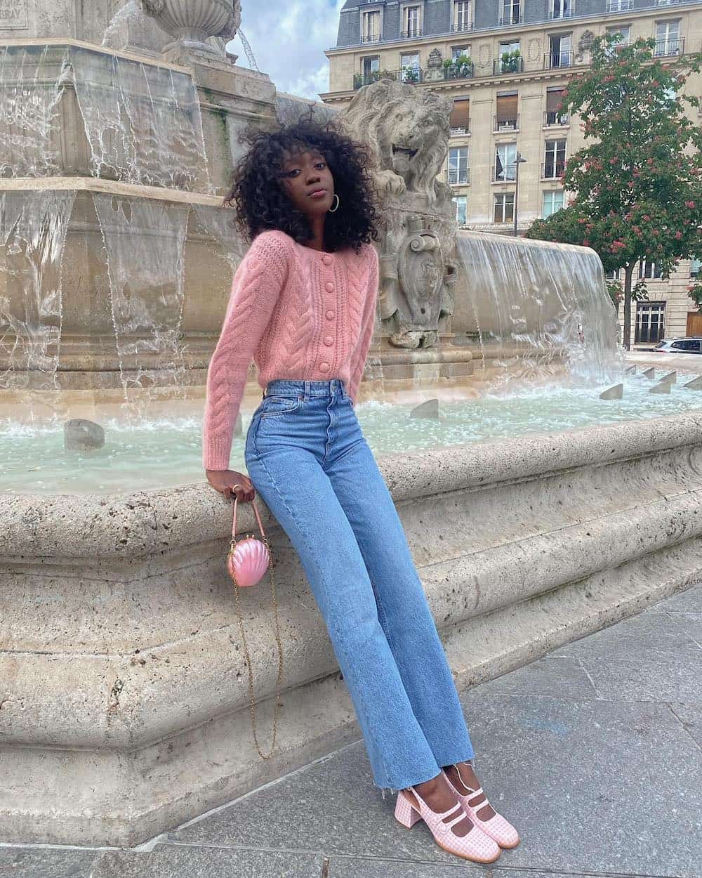 Black woman wearing a pink cardigan with light blue jeans and pink Mary Jane heels