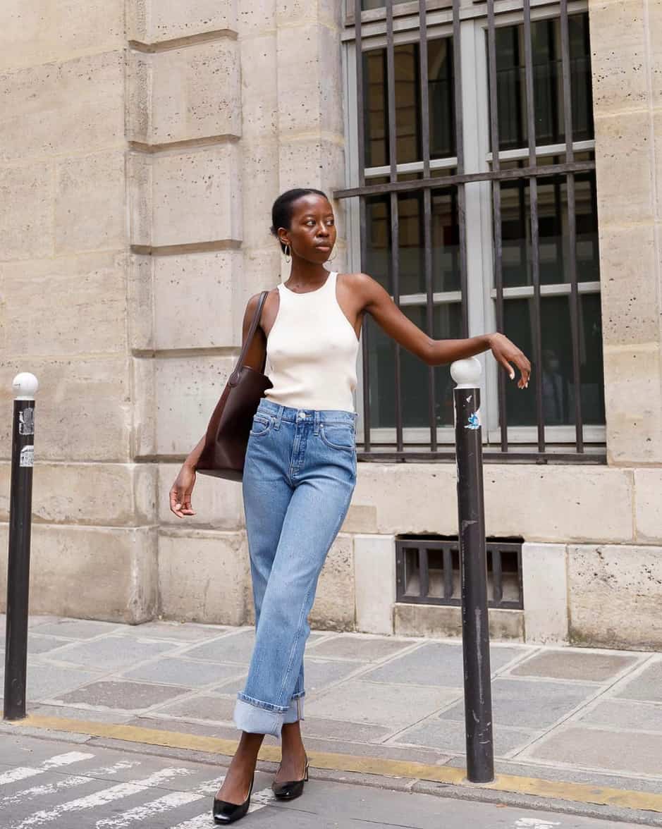 Black woman wearing an ivory tank top with blue jeans with a cuff and black pumps