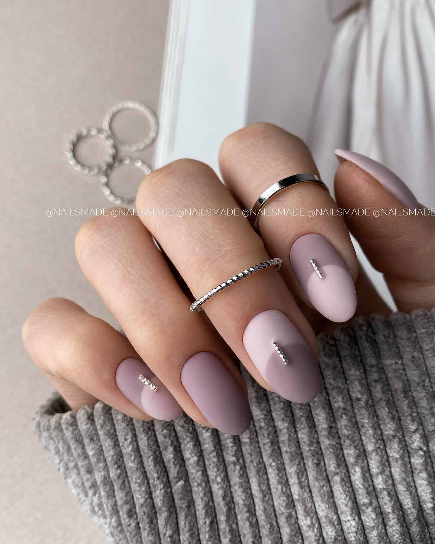 Short, rounded matte mauve manicure. Three nails have light and dark mauve details. Those nails also have gemstones in the middle.