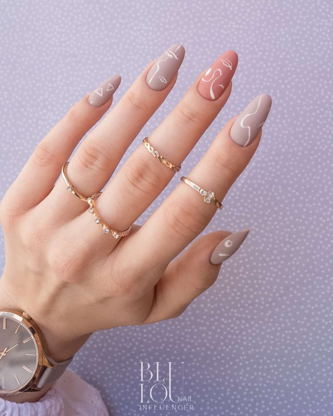 Matte mauve manicure with white thinly lined shapes. The Middle finger is a pinky mauve while the other fingers are a purple mauve.