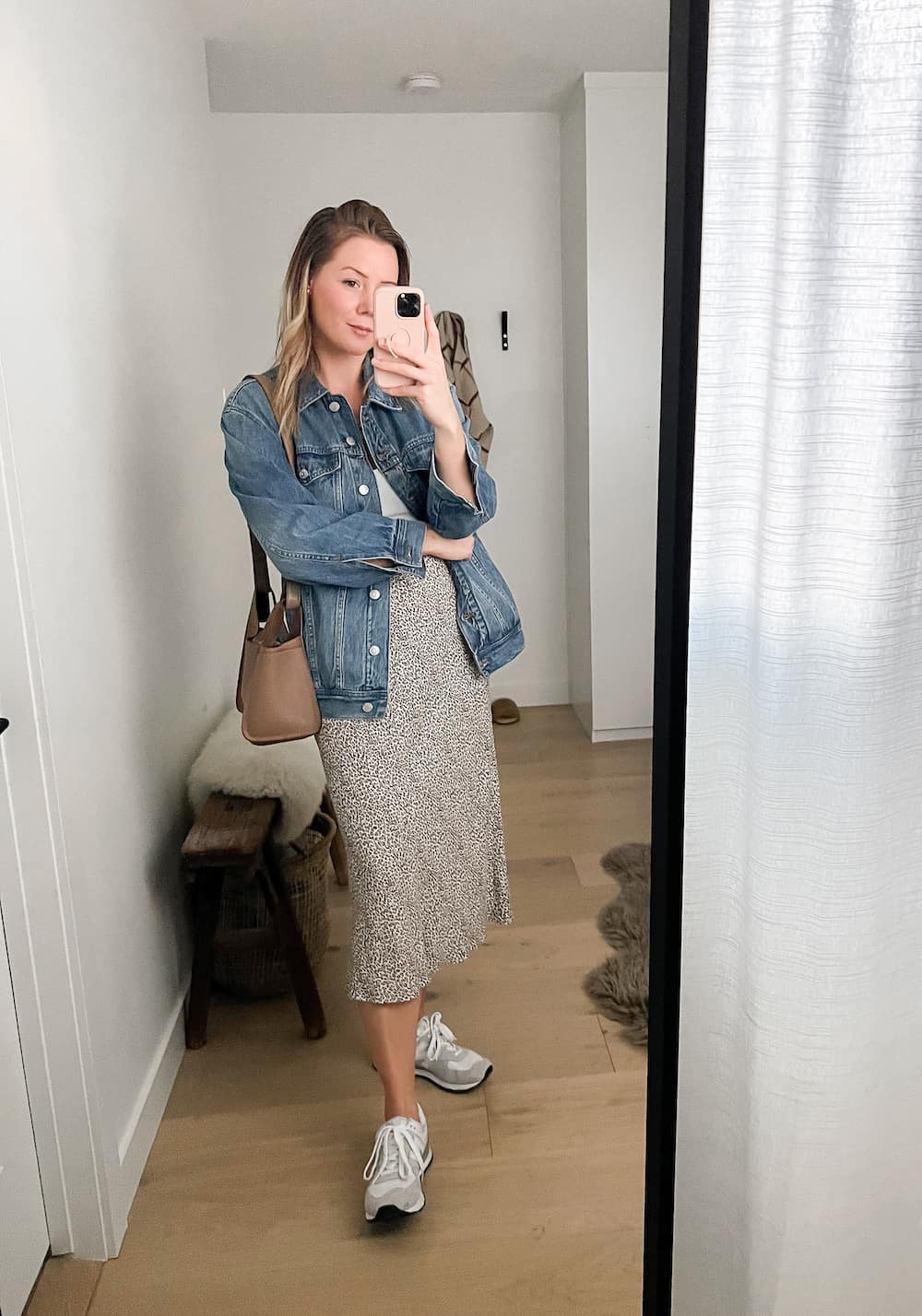 woman wearing an oversized denim jacket, leopard midi skirt, and New Balance 574 sneakers. 