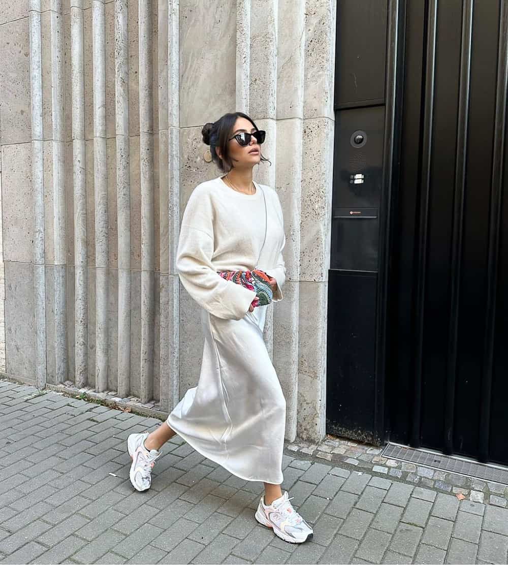 woman wearing an ivory sweater with an ivory silk midi slip skirt and pink New Balance sneakers