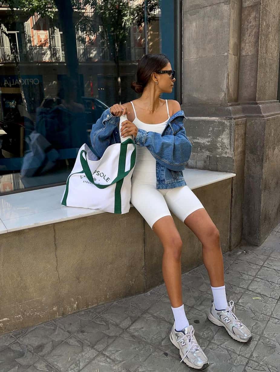 woman wearing a white spandex onesie with an oversized denim jacket, socks, and new balance sneakers