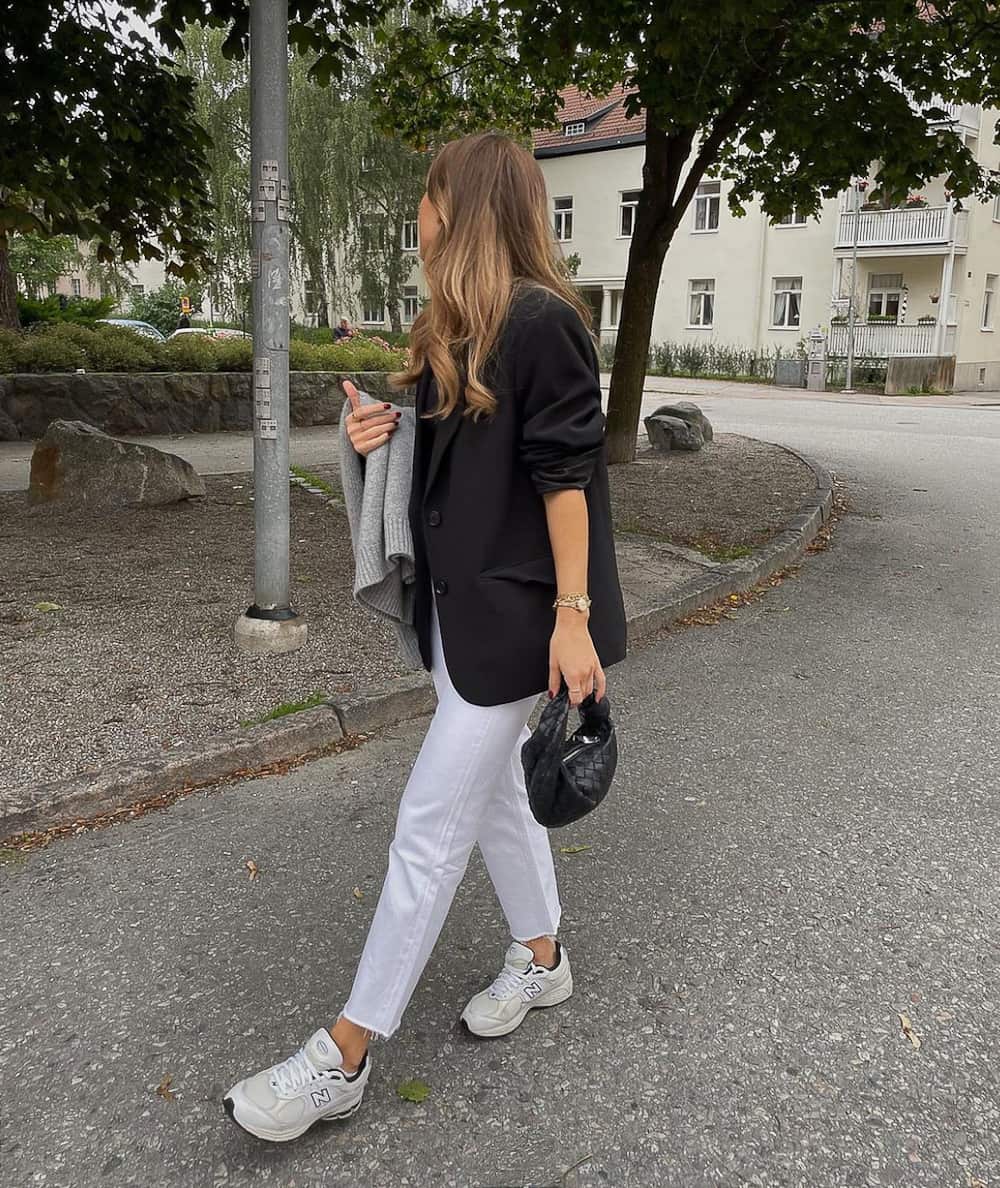 woman wearing a black blazer, white jeans, and New balance sneakers