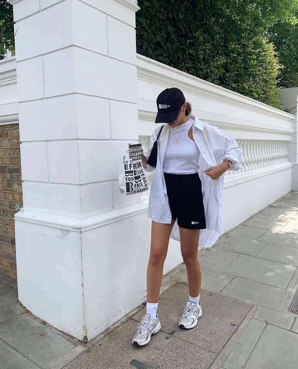 woman wearing an oversized white button up shirt over a white tank and black shorts, with New balance sneakers