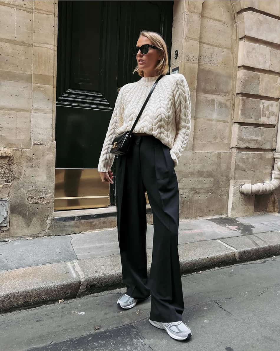 woman wearing a cable knit ivory sweater, wide leg black pants, and new balance sneakers. 