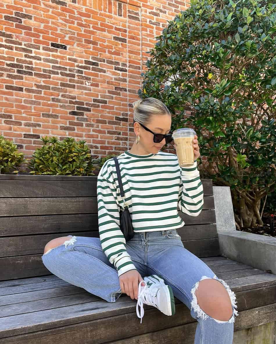 woman wearing a striped green and white top with distressed jeans and white and green New Balance 550 sneakers