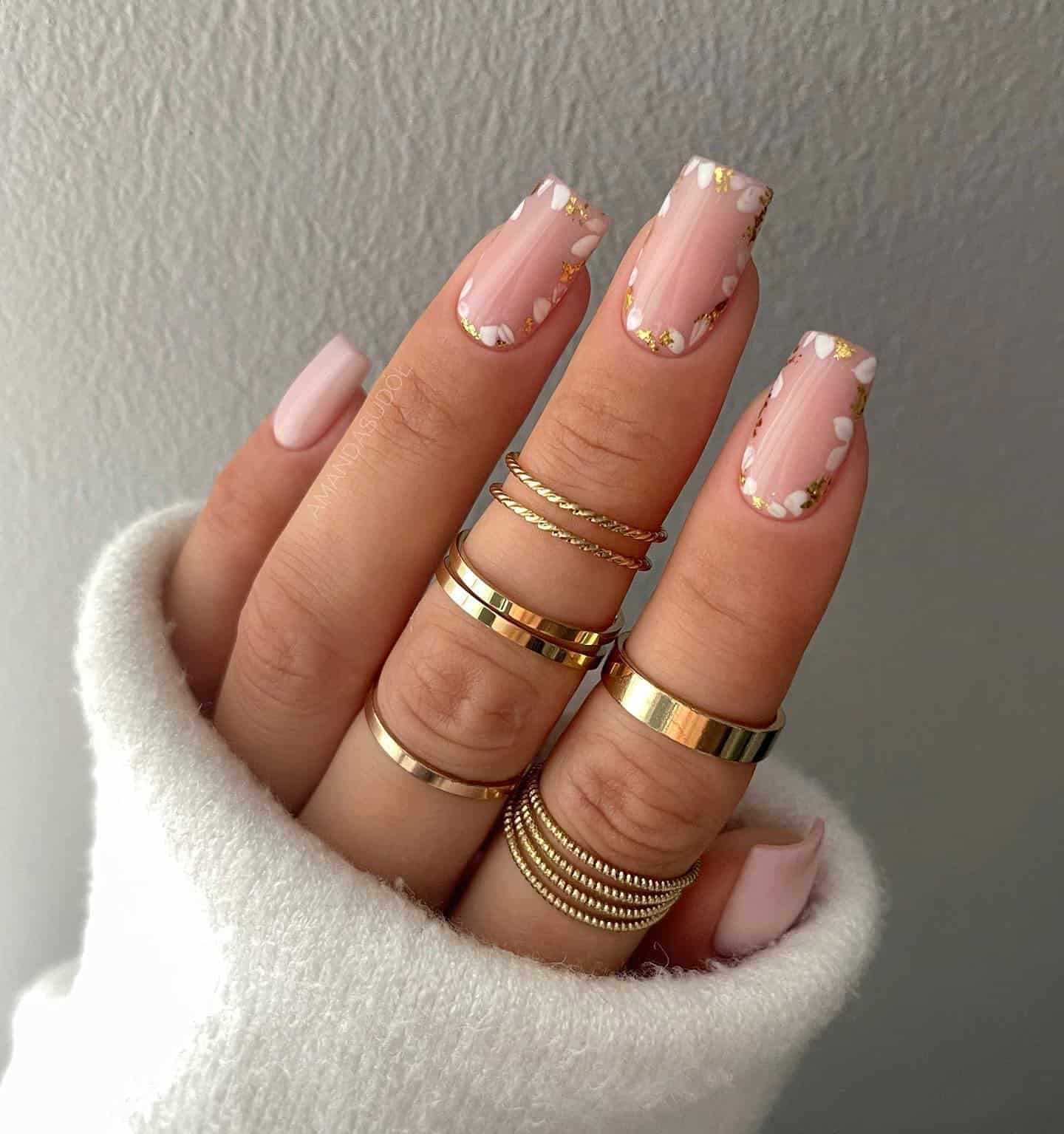 image of a hand with gel nude pink nails with gold flower outline accents