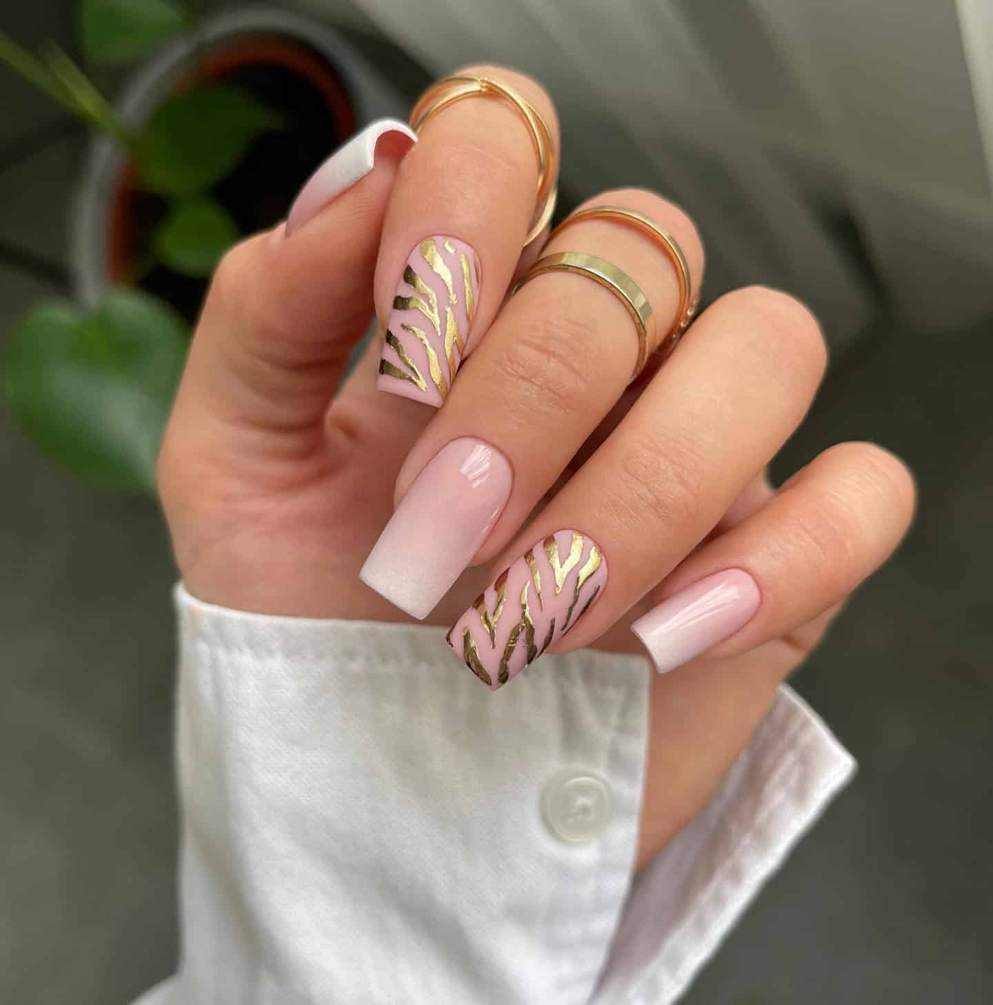 image of a hand with nude pink ombre nails with gold tiger accents on two of the nails