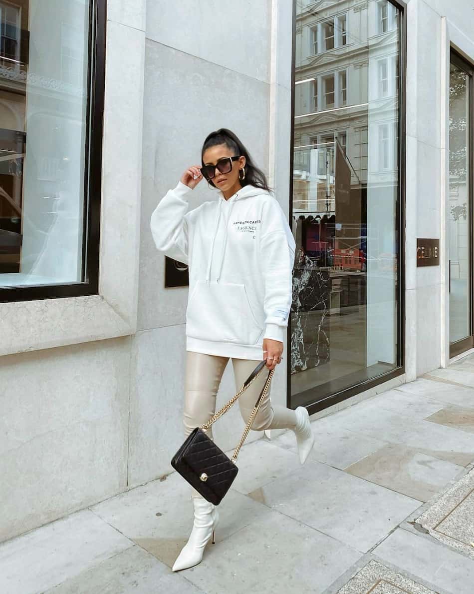 woman wearing an oversized hoodie with cream leather leggings and white ankle boots 
