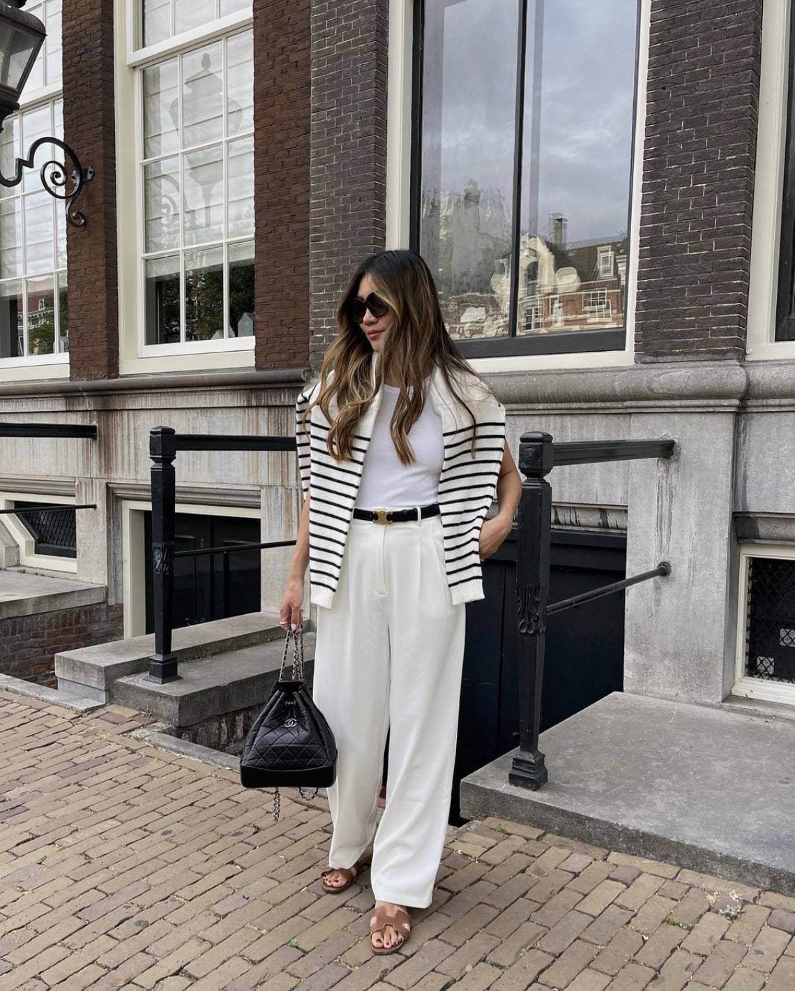French woman wearing a white shirt with white trousers, and a striped shirt over her shoulders