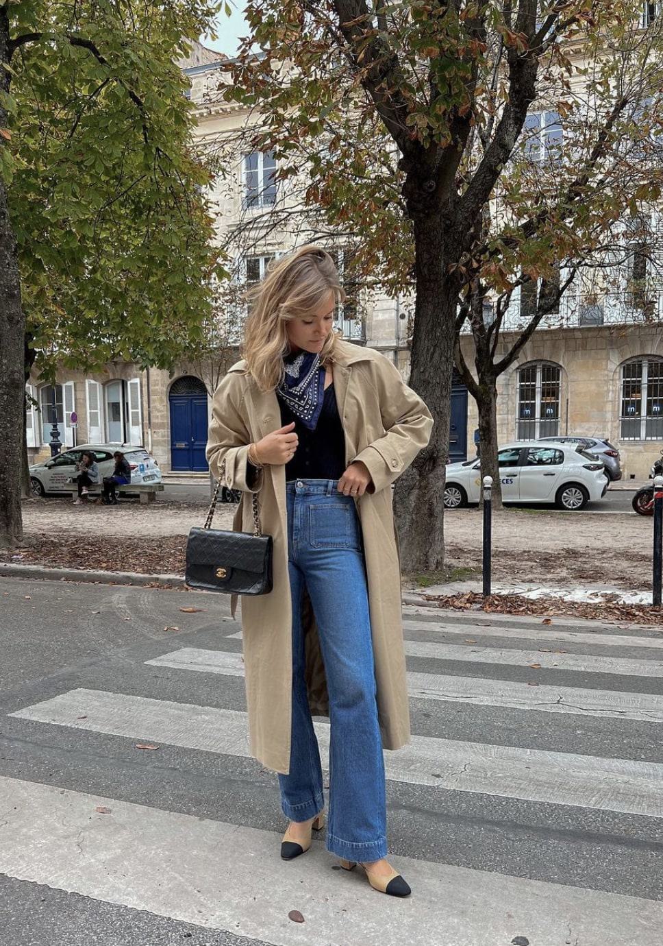 woman in Paris wearing a long trench coat with blue jeans and two-toned flats