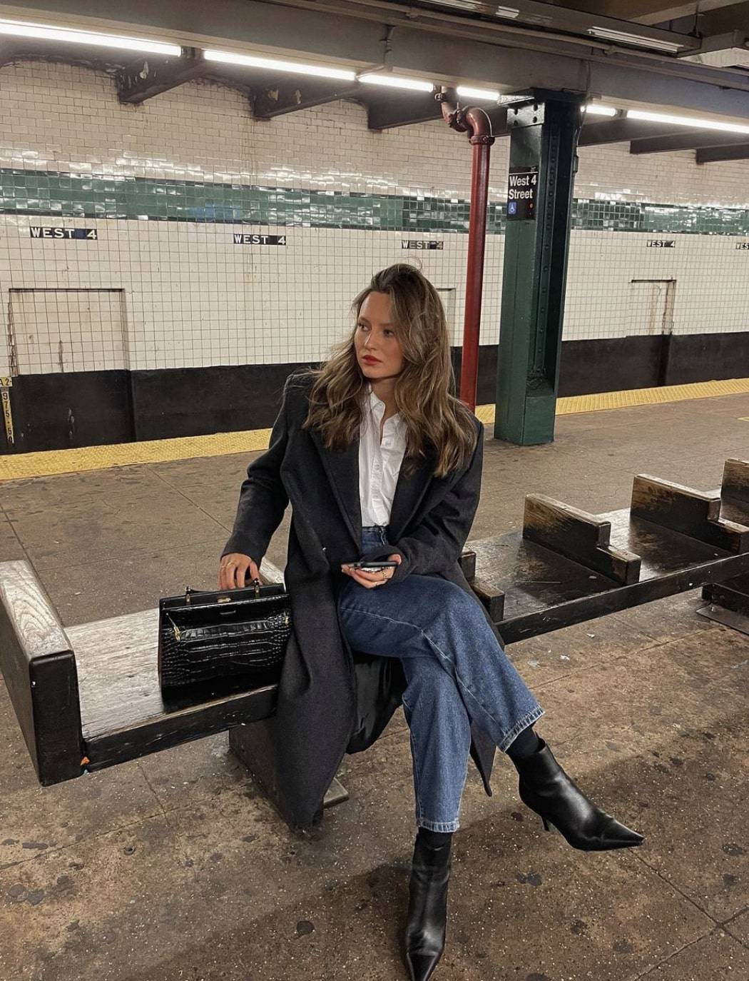 woman wearing a long black coat with blue jeans and pointed black boots