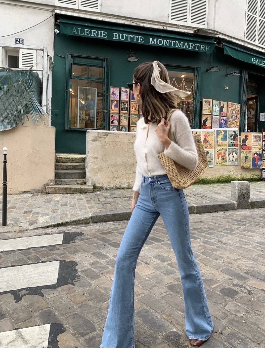 french woman in Paris wearing an ivory cardigan with flared jeans and a bow in her hair