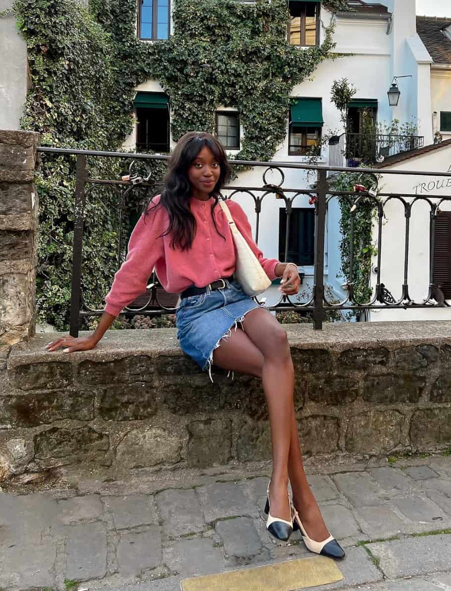 black woman wearing a hot pink cardigan with a denim skirt and Chanel cap-toe heels