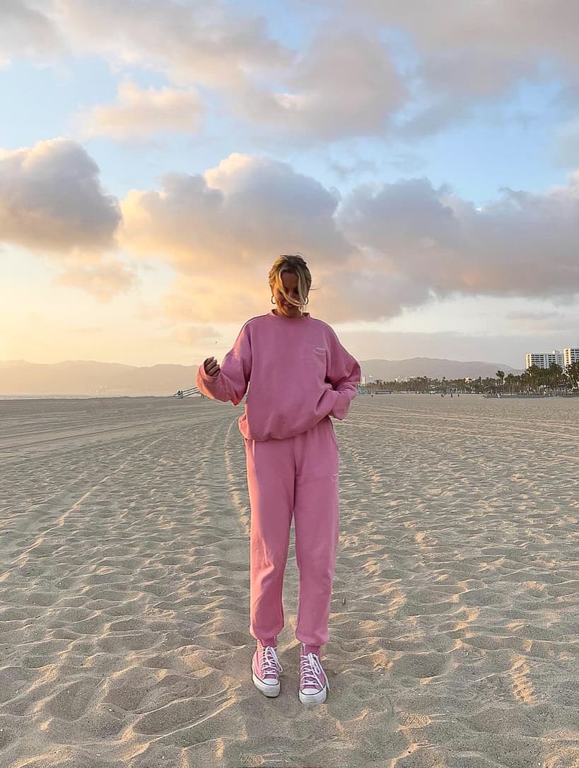 woman standing on the beach wearing a matching pink sweatshirt and sweatpants set with sneakers