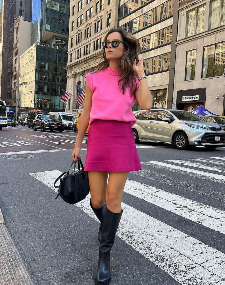 woman wearing a hot pink sweater vest with a pink skirt and black knee-high boots