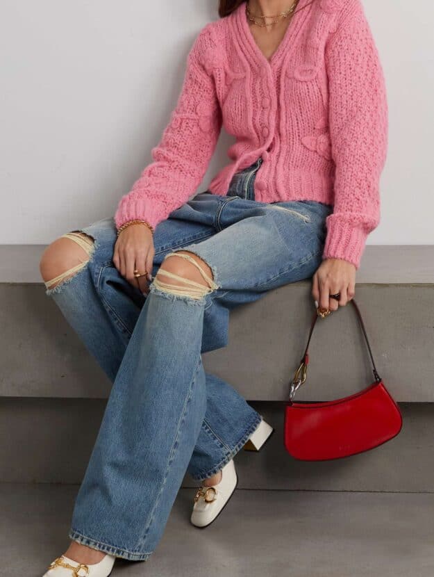 woman wearing a soft pink cardigan with blue bootcut jeans, white Gucci pumps and a red handbag
