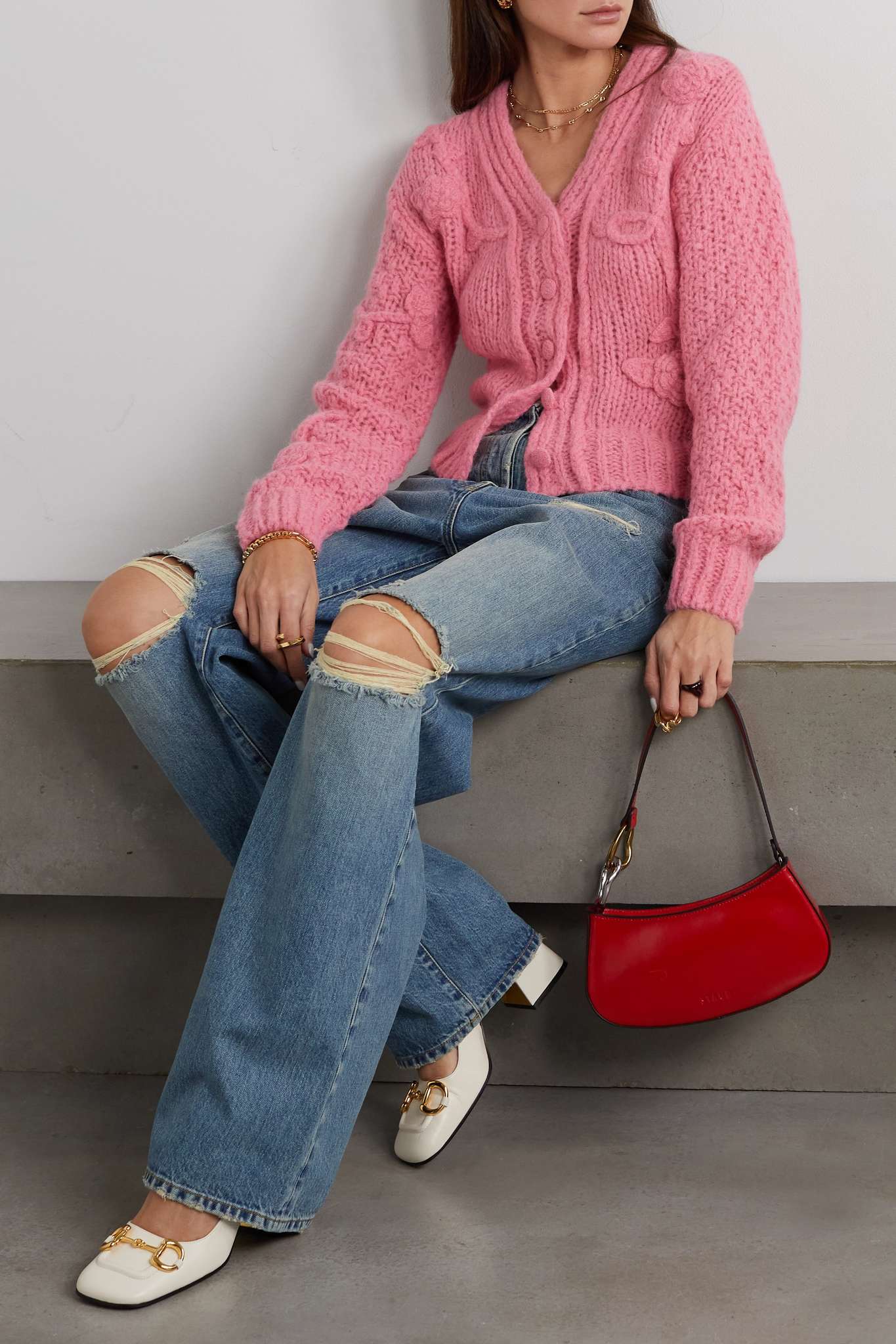 woman wearing a soft pink cardigan with blue bootcut jeans, Gucci pumps and a red handbag