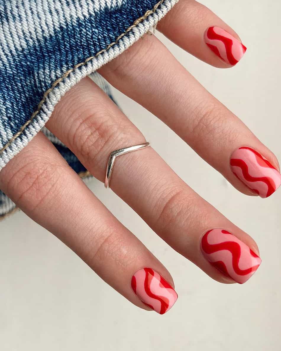 hand with short round natural nails with wavy pink and red designs