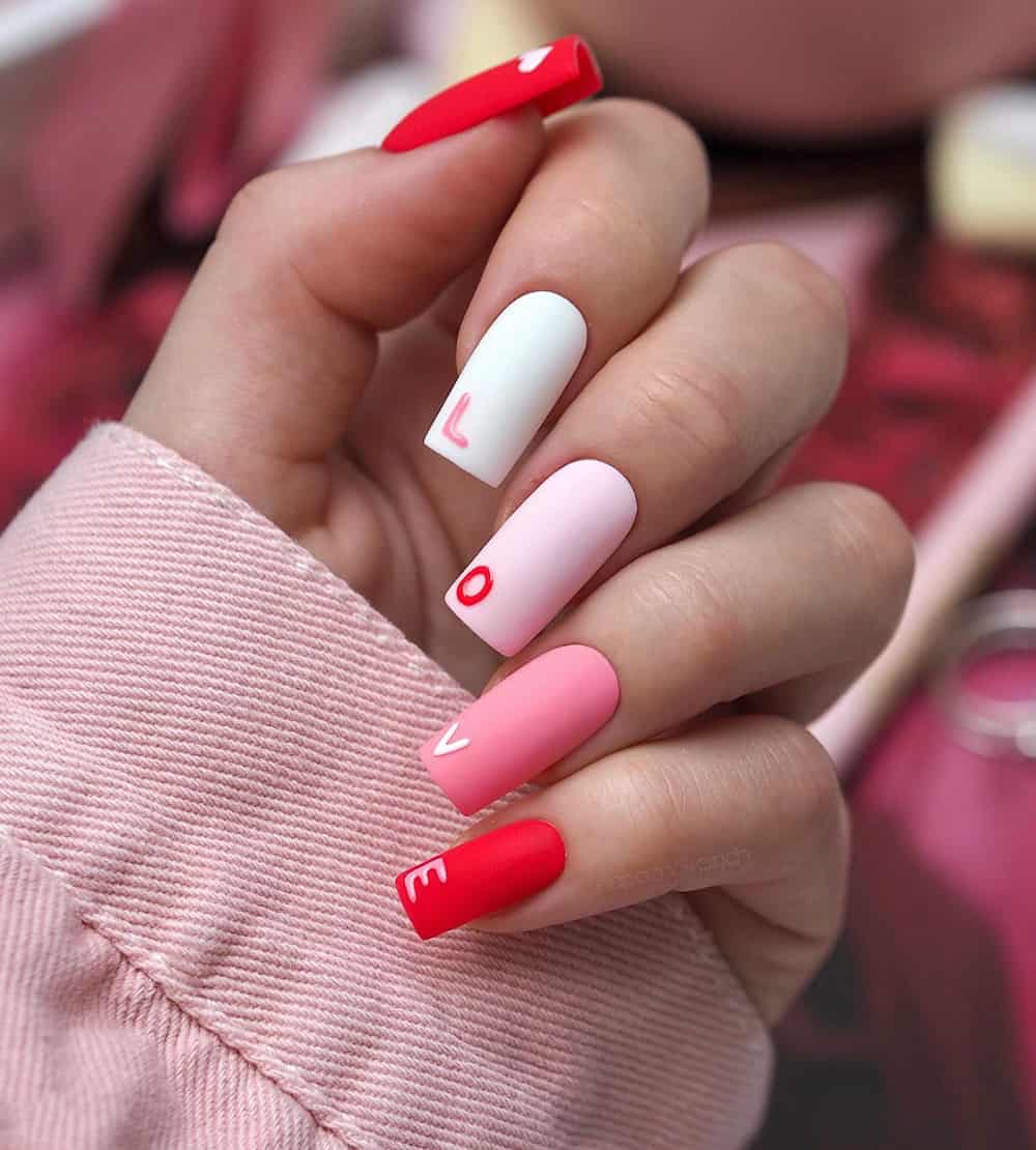 hand with long square acrylic nails with white, pink and red and the word love